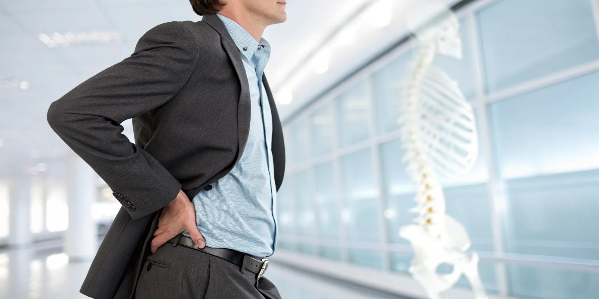 Man holding his lower back in pain from a herniated disc, with a spine model in the background.